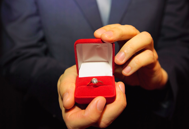 Man in a blue suit gives a ring with a diamond in a red box