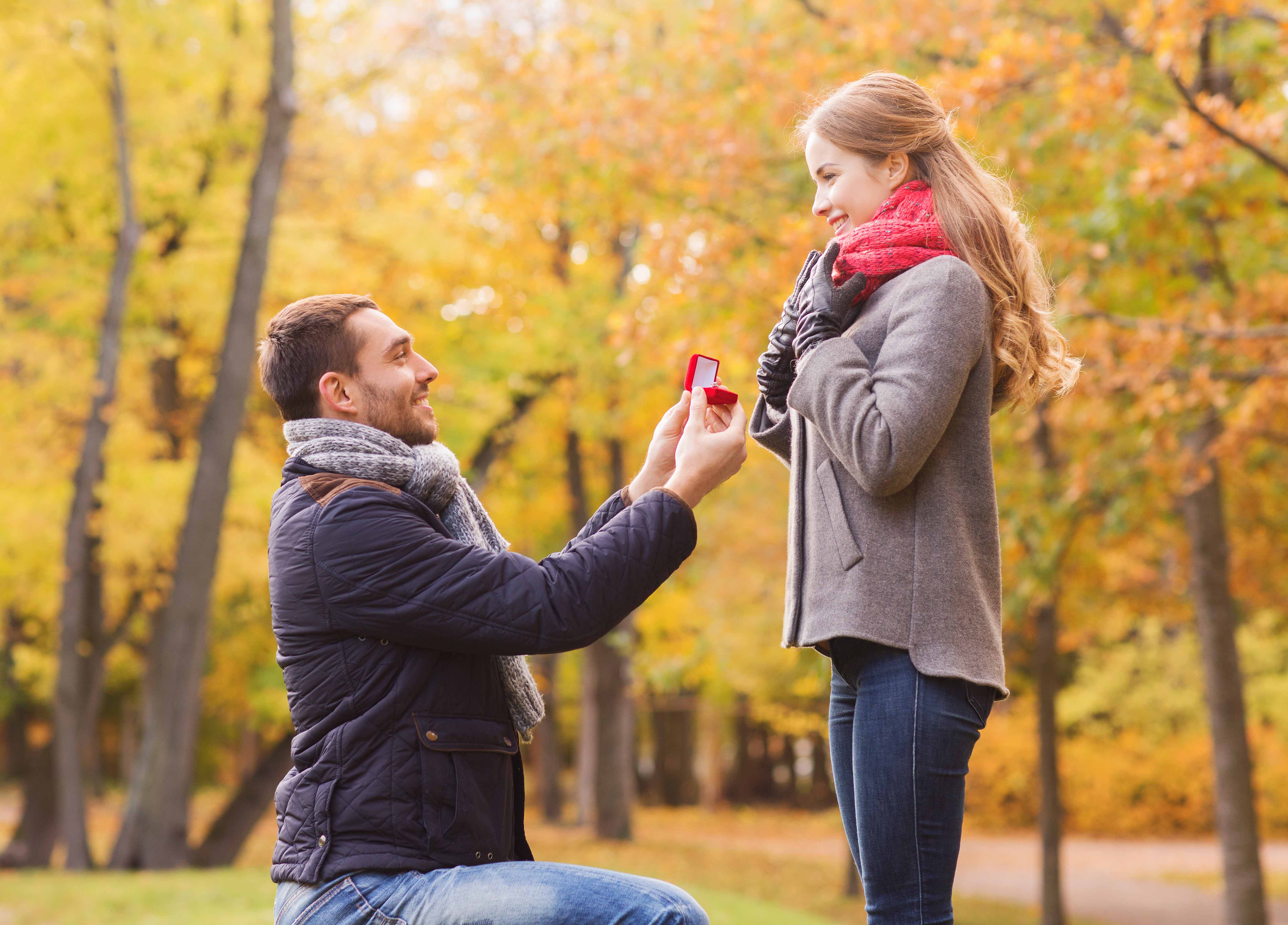 love, family, autumn and people concept - smiling couple with engagement ring in small red gift box outdoors