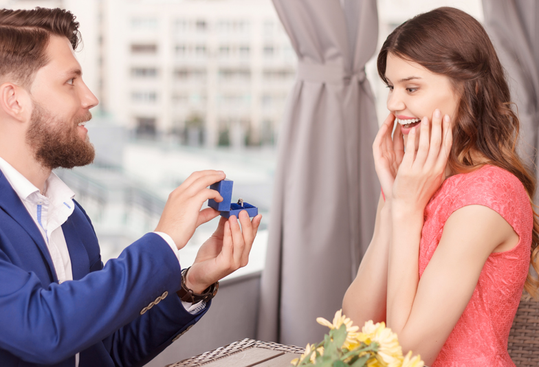 Yes I will. Handsome young man with beard doing proposal to his pretty surprised girlfriend in restaurant.