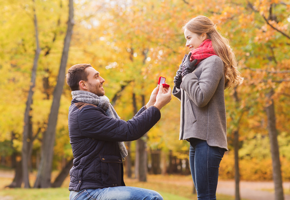 love, family, autumn and people concept - smiling couple with engagement ring in small red gift box outdoors