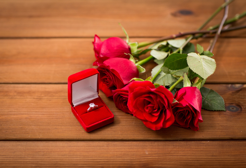 love, proposal, valentines day and holidays concept - close up of gift box with diamond engagement ring and red roses on wood