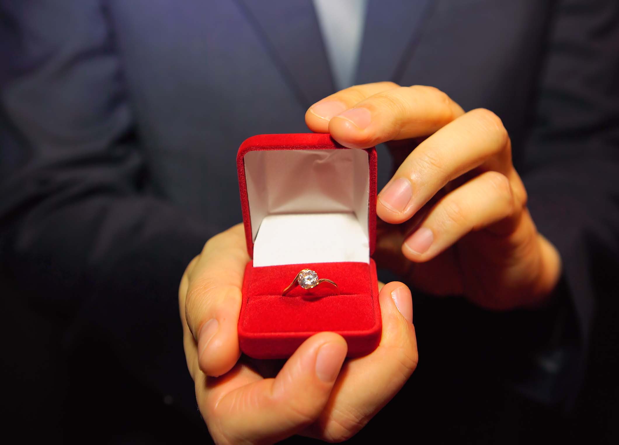 Man in a blue suit gives a ring with a diamond in a red box