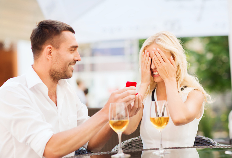 love, proposal, relations, people and holidays concept - happy couple with engagement ring in small red gift box and glasses of wine at restaurant terrace