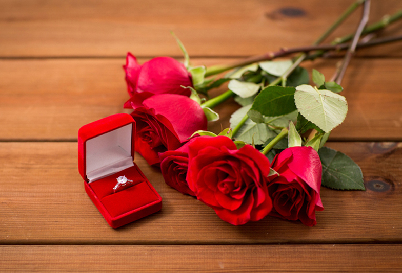 love, proposal, valentines day and holidays concept - close up of gift box with diamond engagement ring and red roses on wood