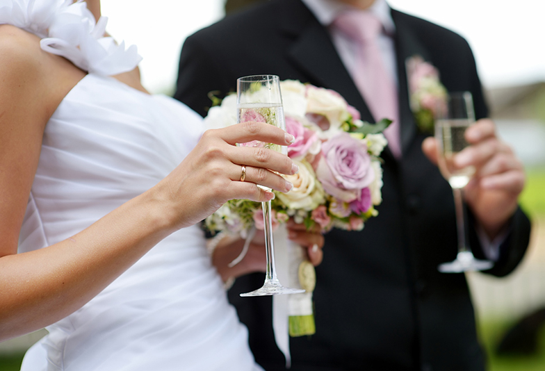 Bride is holding a wedding bouquet and a glass of champagne
