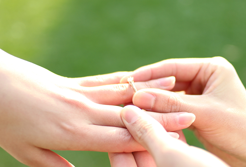 女性の指に婚約指輪をはめる男性の手元