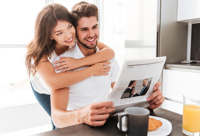 Happy young couple hugging and reading newspaper on the kitchen