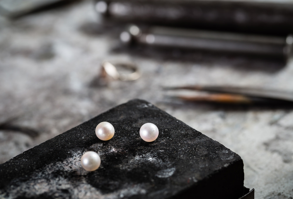 Working desk for craft jewelery making with professional tools and three pearls.